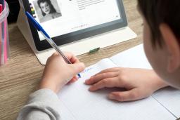 A youth studying at home with a tablet and doing school homework.