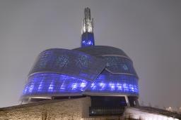 A building surrounded by glass panes illuminated in blue and purple. Snowflake designs are also projected on the windows.