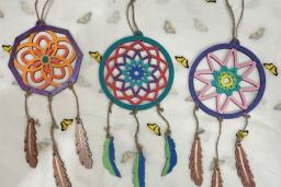 Three colourful dream catchers made from painted wood lie on butterfly-festooned craft paper.