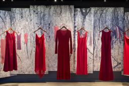 Five red dresses, representing missing and murdered Indigenous women and girls, hang in a row in the Canadian Journeys gallery as part of an exhibit titled “From Sorrow to Strength.” Behind the dresses, the scene of a snow-covered forest with more red dresses hung on the branches of trees is displayed on a series of banners.
