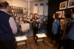 A visitor looks at a gallery niche on residential schools at the Canadian Museum for Human Rights. Two small desks sit in the middle of the niche. A large image of Indigenous students sitting at desks at a residential school is on the back wall of the niche, with images and artifacts on the side walls.