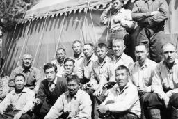 A group of men pose for a picture with a large tent and a tree in the background.