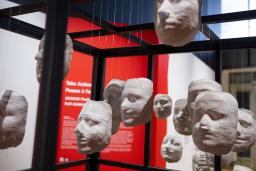 White casts of women’s faces hang by threads from the steel bars of a large cage.