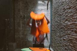 A teenage boy holds a life jacket in his hands while he stands behind a dome-like structure made of lifejackets.