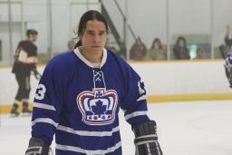 Un jeune homme portant un uniforme de hockey bleu orné d'un logo de couronne sur une patinoire intérieure.