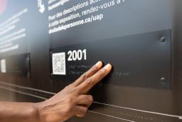 A hand touches braille letters on a museum exhibit.