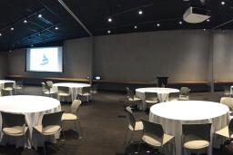 Circular tables with white tablecloths and seating in a large room, with a screen showing the Museum logo on the far wall.