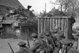 A group of armed soldiers watch a tank drive past.