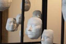 Several white plaster faces hang from strings, inside a cage.