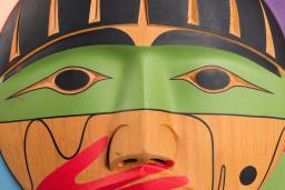 A carved wooden box, showing the carved face of a person with a painted red hand over their mouth.