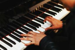 Two hands play the keys of a gleaming black Yamaha piano. The pianist, barely shown, wears a long-sleeved black top.