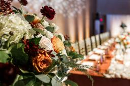 A bouquet of roses is in the foreground with a head table arrangement in the background.