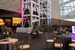 Round tables and chairs are set up for an evening reception around an indoor rock garden.