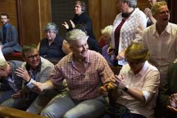 A group of people are cheering and applauding while sitting in a courtroom on wooden benches.