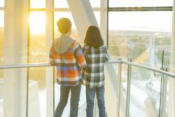 Two young children stand in a tower with their backs toward the camera as they stare out at a horizon overlooking a cityscape.