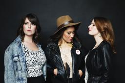 Three women pose in front of a black wall.