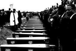 People stand in front of a row of coffins.
