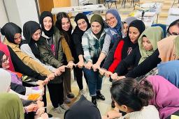 A group of smiling Muslim women in a circle with linked hands.