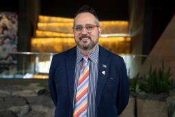 Walter Cassidy stands in front of the glowing alabaster ramps at the Canadian Museum for Human Rights. On his suit lapel, a small pin reads "Queer."