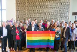 Twenty-eight members of the LGBT Purge Fund Board and LGBTQ2+ National Monument Advisory Committee standing together and holding a rainbow flag, at the first Monument visioning session in 2019.