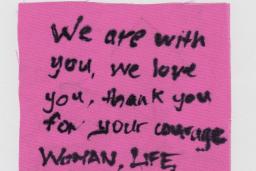 Piece of cloth with "We are with you, We love you, Thank you for your courage Woman, Life, Freedom" written with a black marker.
