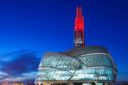 A huge building with a rounded glass façade is topped by a glowing red tower.