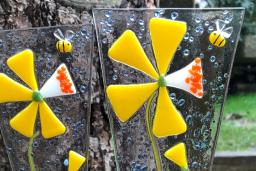 Two fused glass ornaments depicting yellow flowers sit in a flower pot outside.