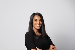 A portrait of a smiling woman standing with arms crossed in front of a white backdrop.