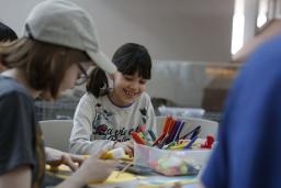 Children of different ages are sitting around a table doing crafts.