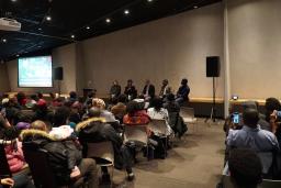 A panel of five people are seated in front of a large crowd inside the Canadian Museum for Human Rights.