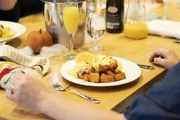 A person is sitting at a table with a glass of orange juice and a plate of eggs benedict and hash browns.
