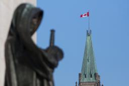 A Canadian flag flies atop a large tower. In the foreground stands a statue of a veiled woman carrying a sword.