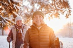 An older couple is walking through a wooded area using nordic poles.