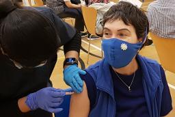 A healthcare worker prepares to give a vaccine to a patient. Both people are wearing medical face masks. 