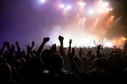 Concert-goers raise their hands in collective jubilation as a band plays on a brightly lit stage.