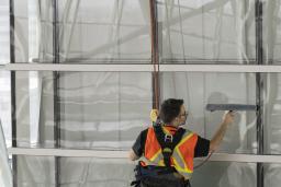 Male worker wearing safety vest suspended from ropes cleaning windows from a high height.