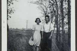 A young Japanese Canadian couple pose in a field with trees in the background.