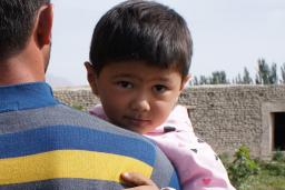A young child being carried by an adult looks back over the adult’s shoulder.