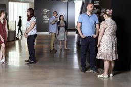 Small groups of people stand in a Museum exhibition space and talk to one another.