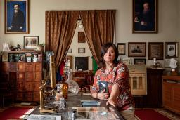 A woman kneels beside a coffee table surrounded by books and heirlooms.