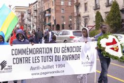 A group of people walking down a street with sign that reads “Commémoration du génocide contre les Tutsi du Rwanda. Avril-Juillet 1994. www.pagerwanda.ca”.