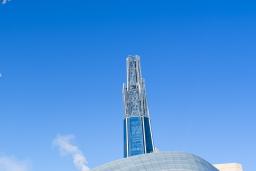 An outdoor winter scene with an exterior view of the Canadian Museum for Human Rights, other buildings in the distance and trees covered in frost.