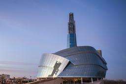 The exterior of the Canadian Museum for Human Rights, seen in the sunset against the city skyline.