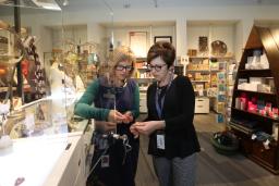 Two women look at a piece of jewellery. They are standing in a store full of colourful merchandise.