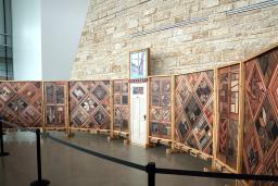 Right view of a structure of vertical wood panels covered in patterns of images, with a white wooden door at the centre.