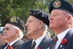 Three older men in Canadian Legion uniforms sit beside each other. They are all wearing Remembrance Day poppies on their uniforms.