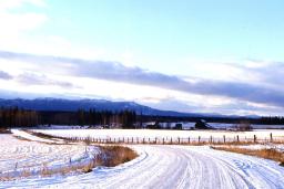 A snow-covered country road with mountains in the background.