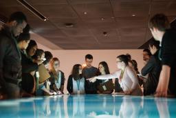 A group of young people stand around an interactive table emitting blue and white light.