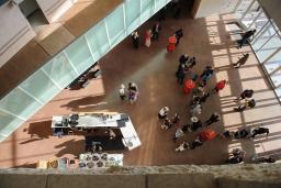 A bird’s-eye view of a crowd of people gathered in a large open area in the Museum. There are cocktail tables with red tablecloths and a bar on the left side of the image.