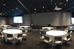 Circular tables with white tablecloths and seating in a large room, with a screen showing the Museum logo on the far wall.